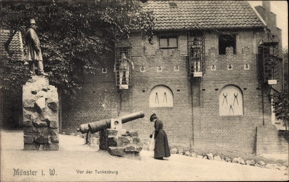 Ak-Muenster-in-Westfalen-Vor-der-Tuckesburg-Denkmal-Geschuetz-Strafkaefige-an-der-Burgmauer.jpg