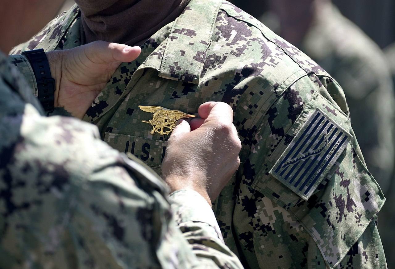 1280px-Commander_places_a_special_warfare_pin_on_a_member_of_SEAL_Qualification_Training_Class_336_during_a_graduation_ceremony._(49783931948).jpg